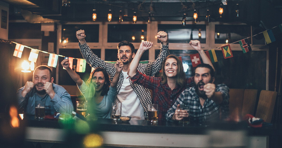 5 Personen sitzen an Bar und jubeln zu einem Fussballspiel